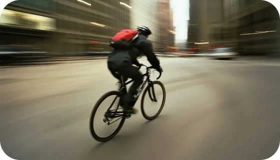 Cyclist wearing a helmet and red backpack riding a bicycle fast through an urban street with motion blur.