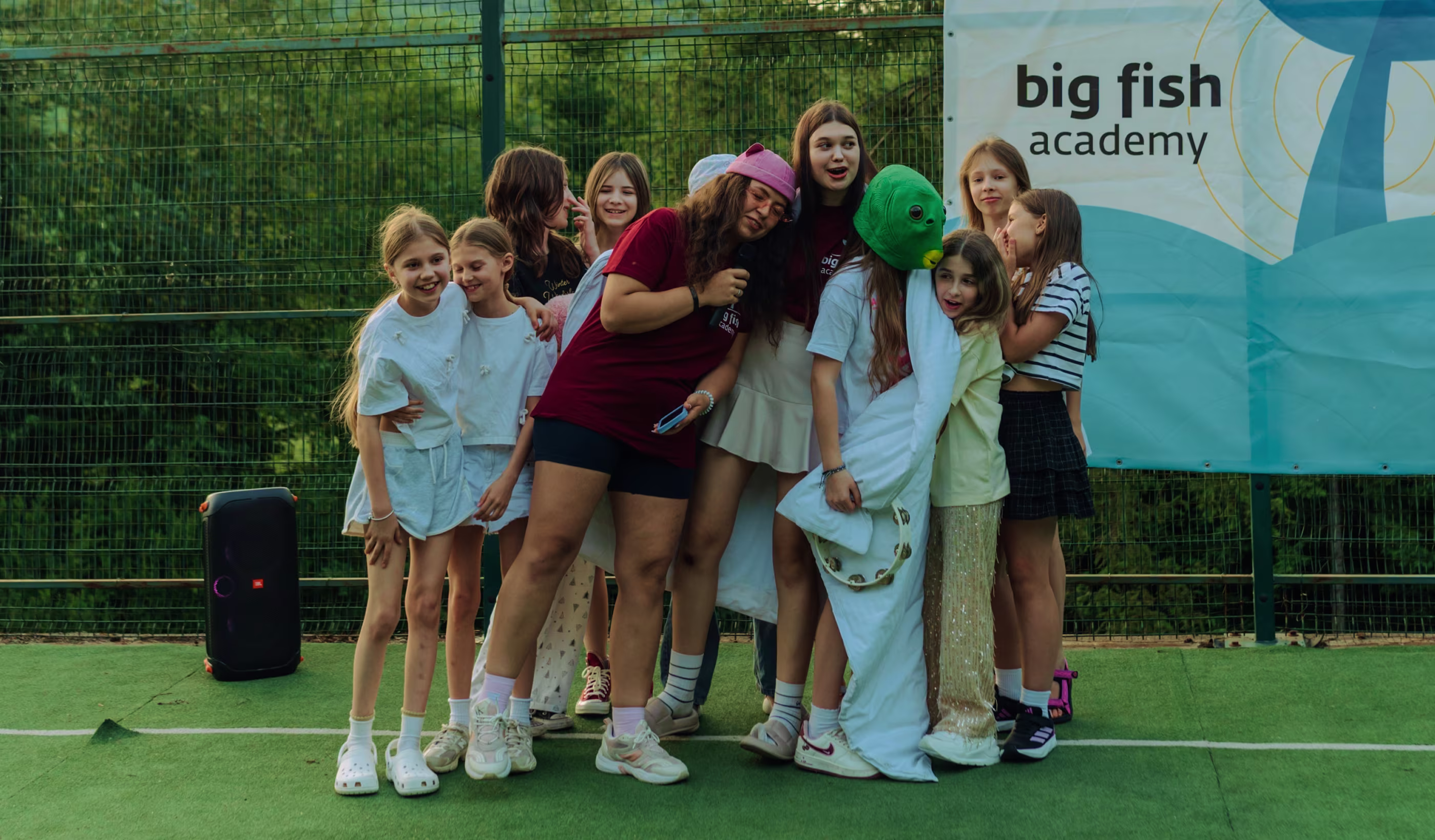 Група дітей і підлітків разом на спортивному майданчику біля банера з написом big fish academy.