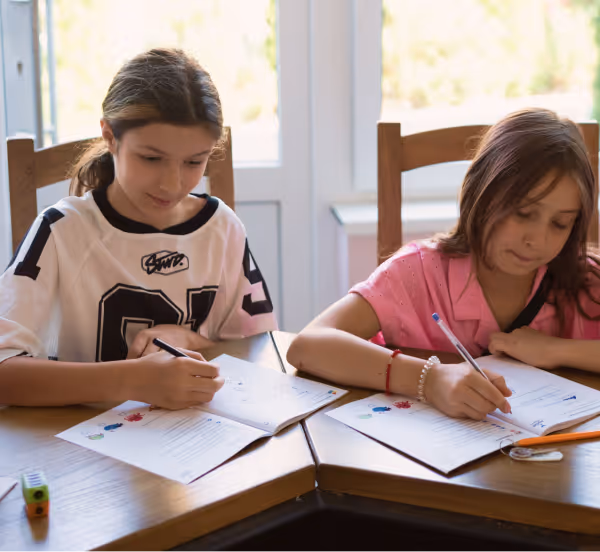 Дві дівчинки сидять за столом і роблять домашнє завдання з підручниками та зошитами.