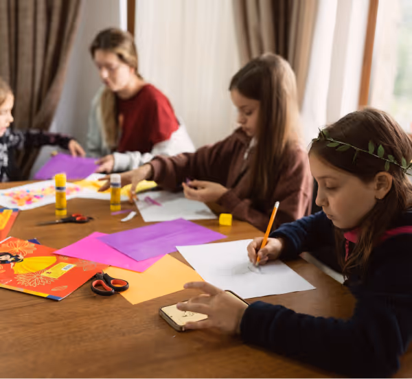 Діти за столом займаються творчістю з кольоровим папером, клеєм і олівцями.