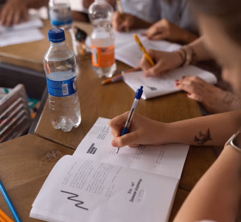 Люди заповнюють анкети або документи ручками на дерев'яному столі з пластиковими пляшками води.