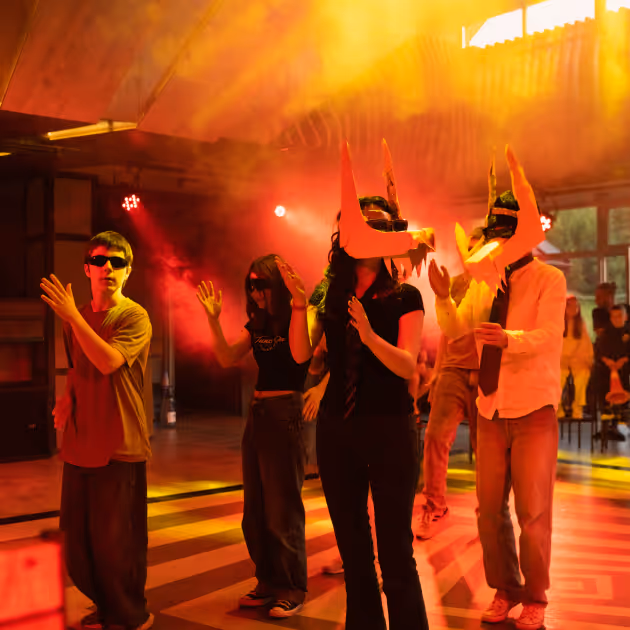 Група молодих людей танцює під червоне світло на вечірці, двоє у масках з довгими рогами.