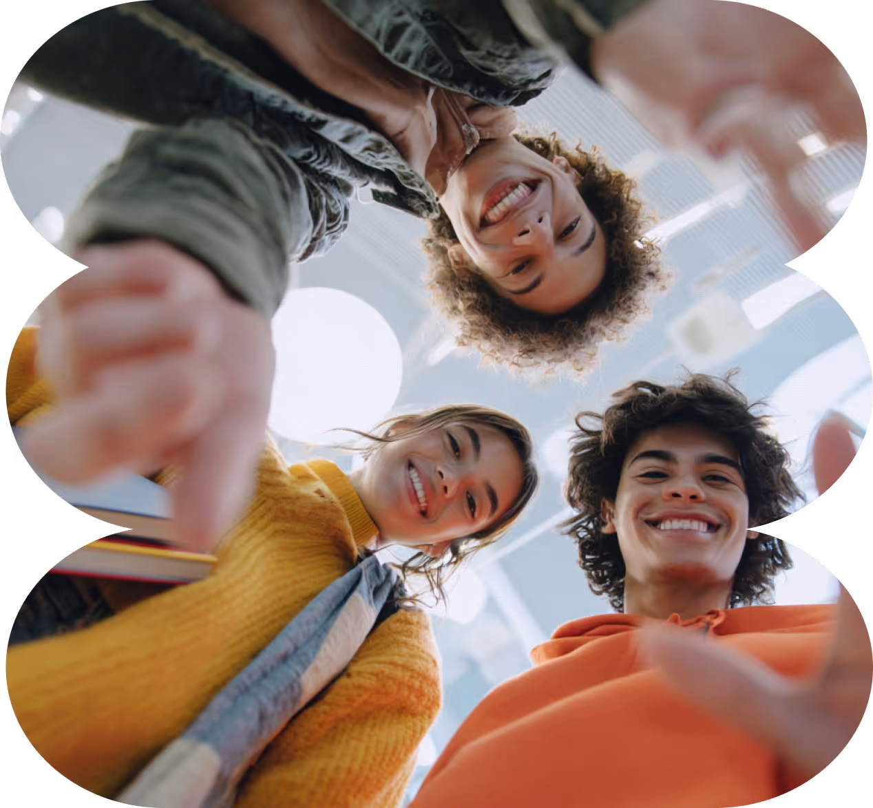 Три молоді людини у яскравому одязі стоять у колі, усміхаються та дивляться вниз задоволеними.