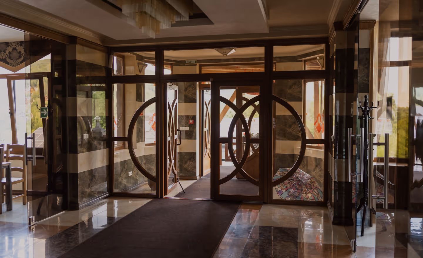 Інтер'єр входу з мармуровою підлогою, дерев'яними дверима з круглими візерунками та розкладеним парасолькою біля стіни.