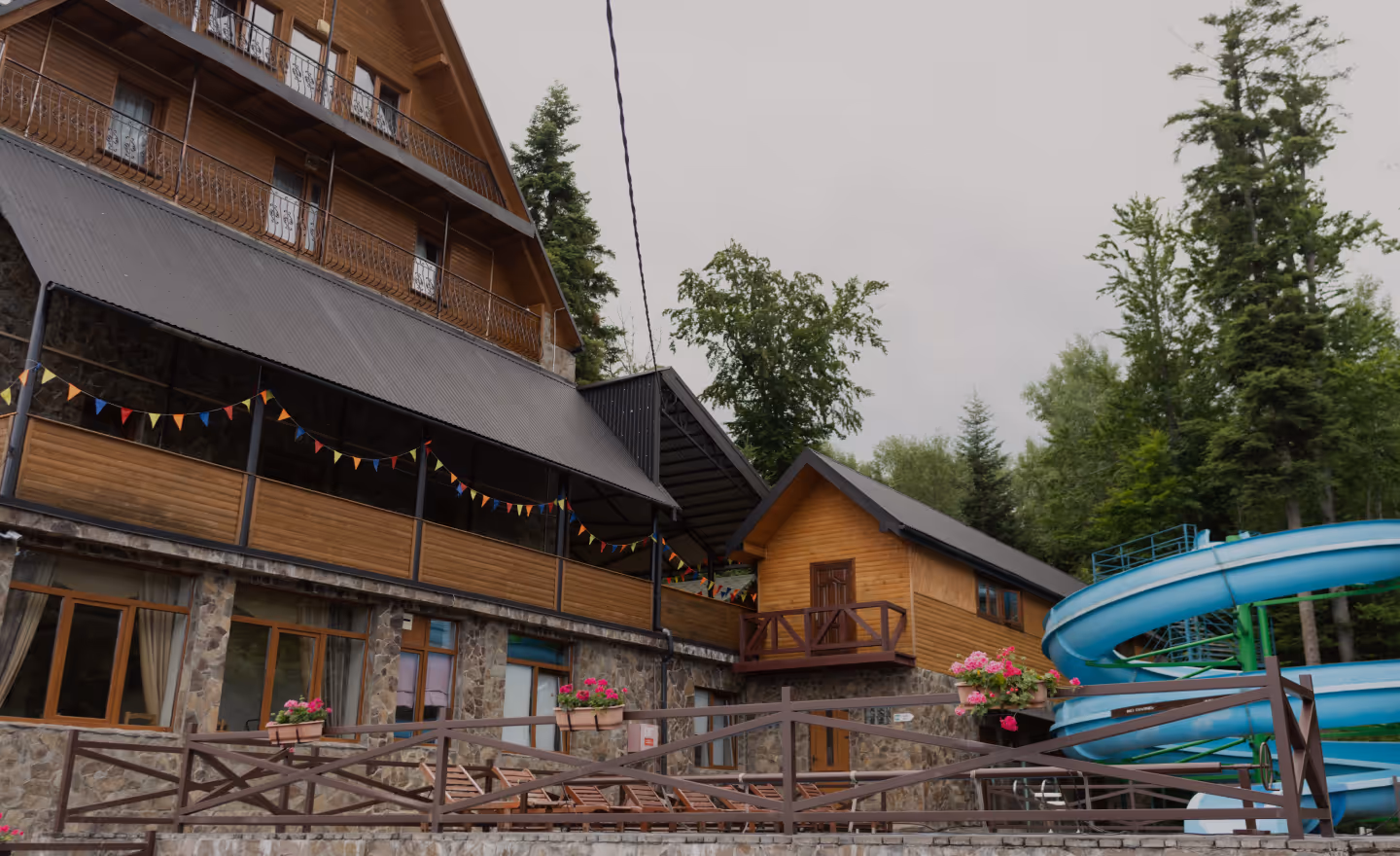 Дерев'яний готель зі спортивною гіркою та ялинками навколо в похмурий день.