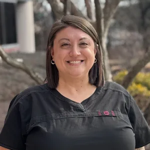 Smiling woman with blonde hair and glasses wearing a black top against a plain background.