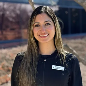 Smiling woman with long dark hair wearing a black top against a plain light background.