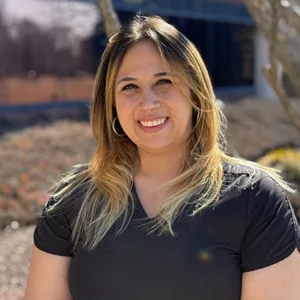 Smiling woman with long blonde hair wearing a black top against a beige background.
