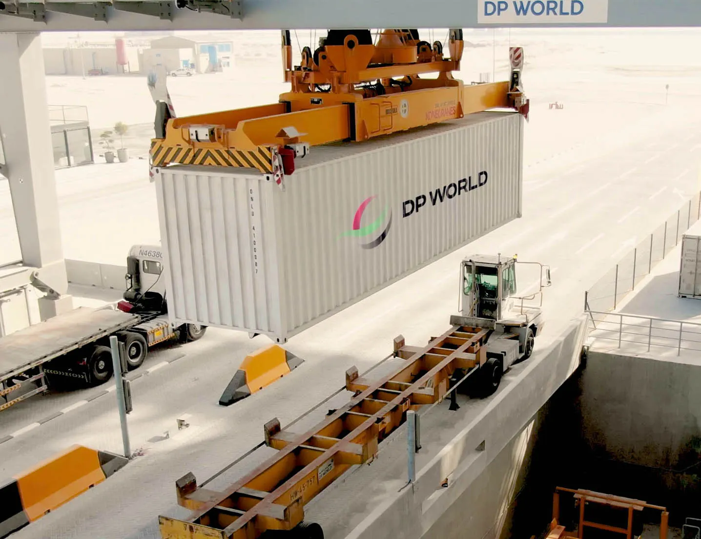 White DP World shipping container being lifted by an orange crane onto a white container truck in a port area.