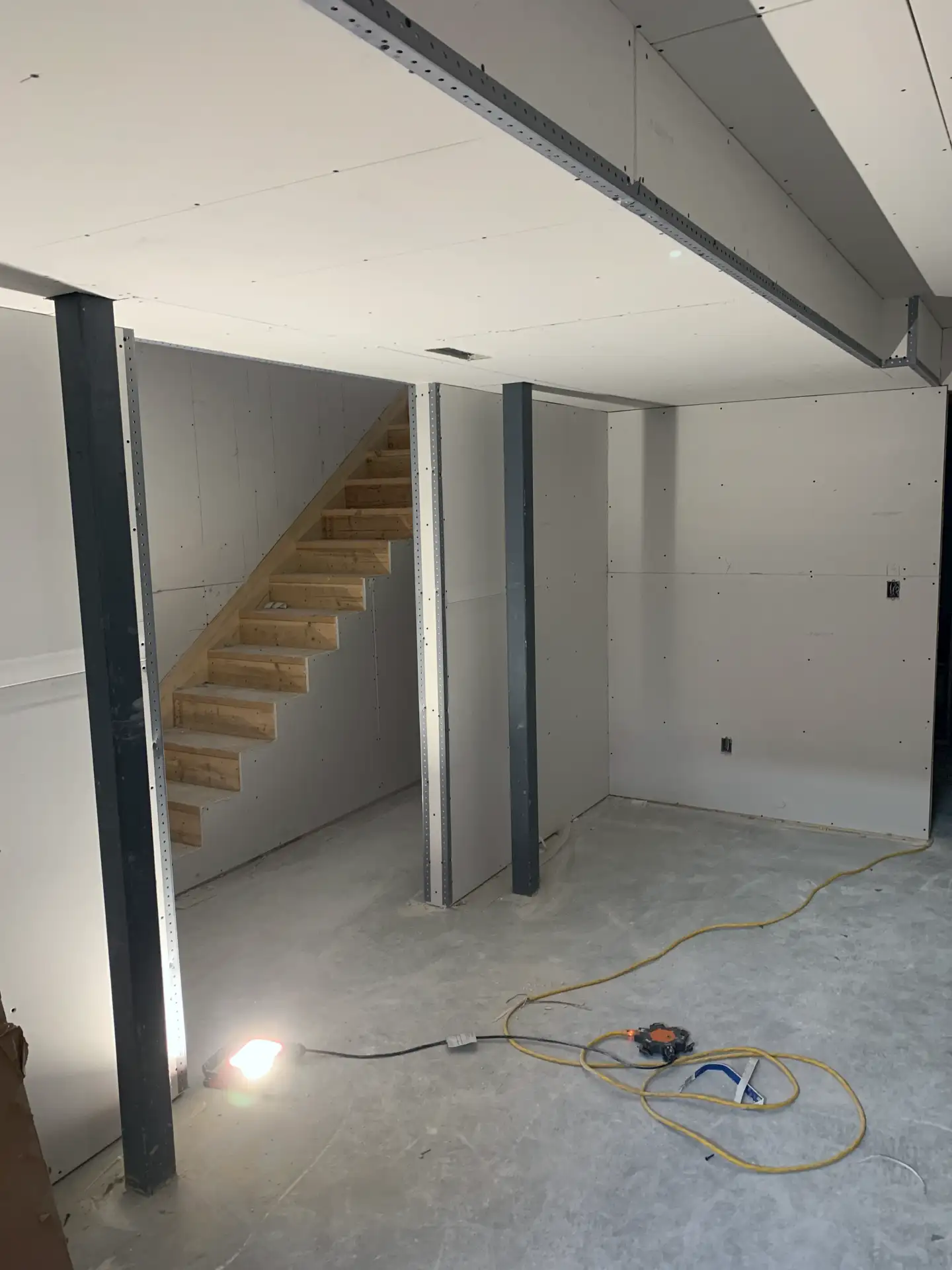 Drywall and corner beads installed in the basement finish project. Portion of the ceiling, bulkhead and staircase visible.