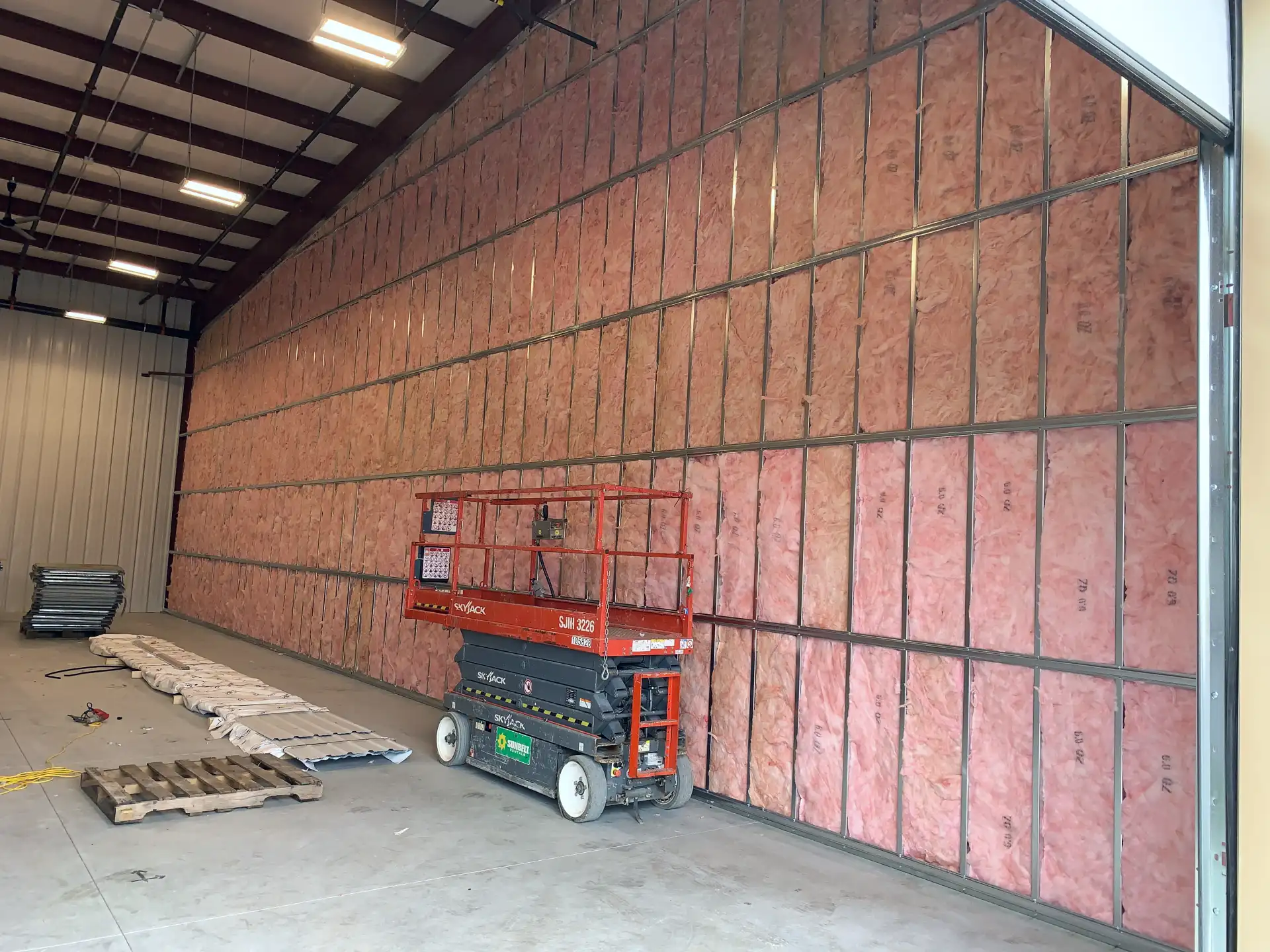framed tall partition dividing the warehouse with insulation and resilient channel installed. Scissor lift is parked in front of the wall.