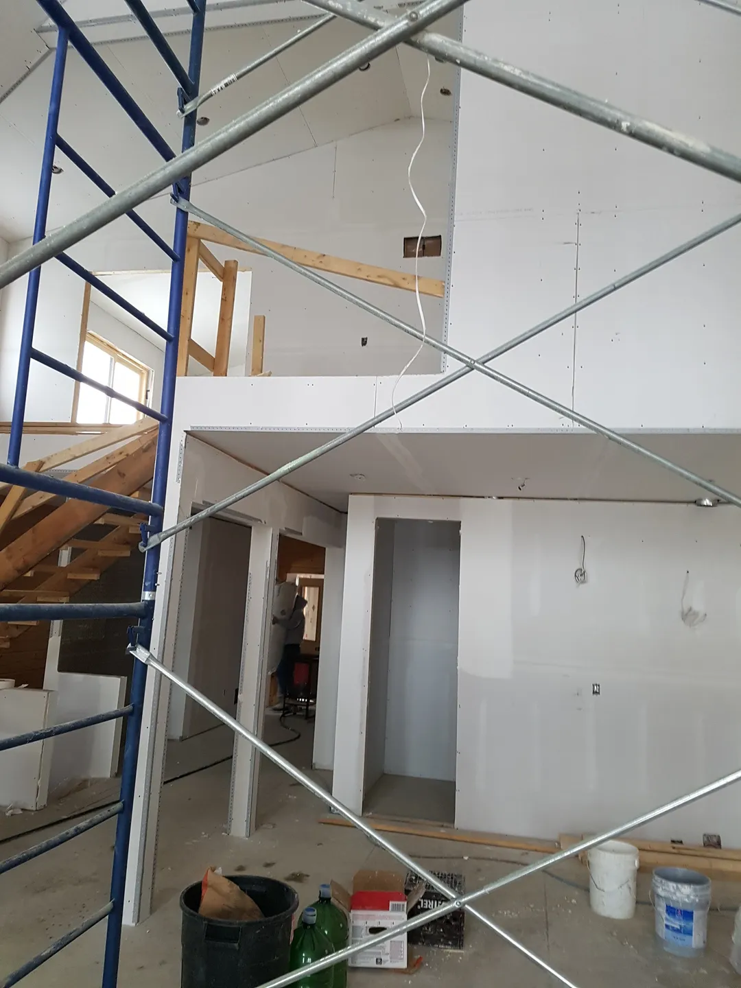 Tall blue metal scaffolding on wheels inside a room under construction with wood-paneled wall and drywall ceiling.