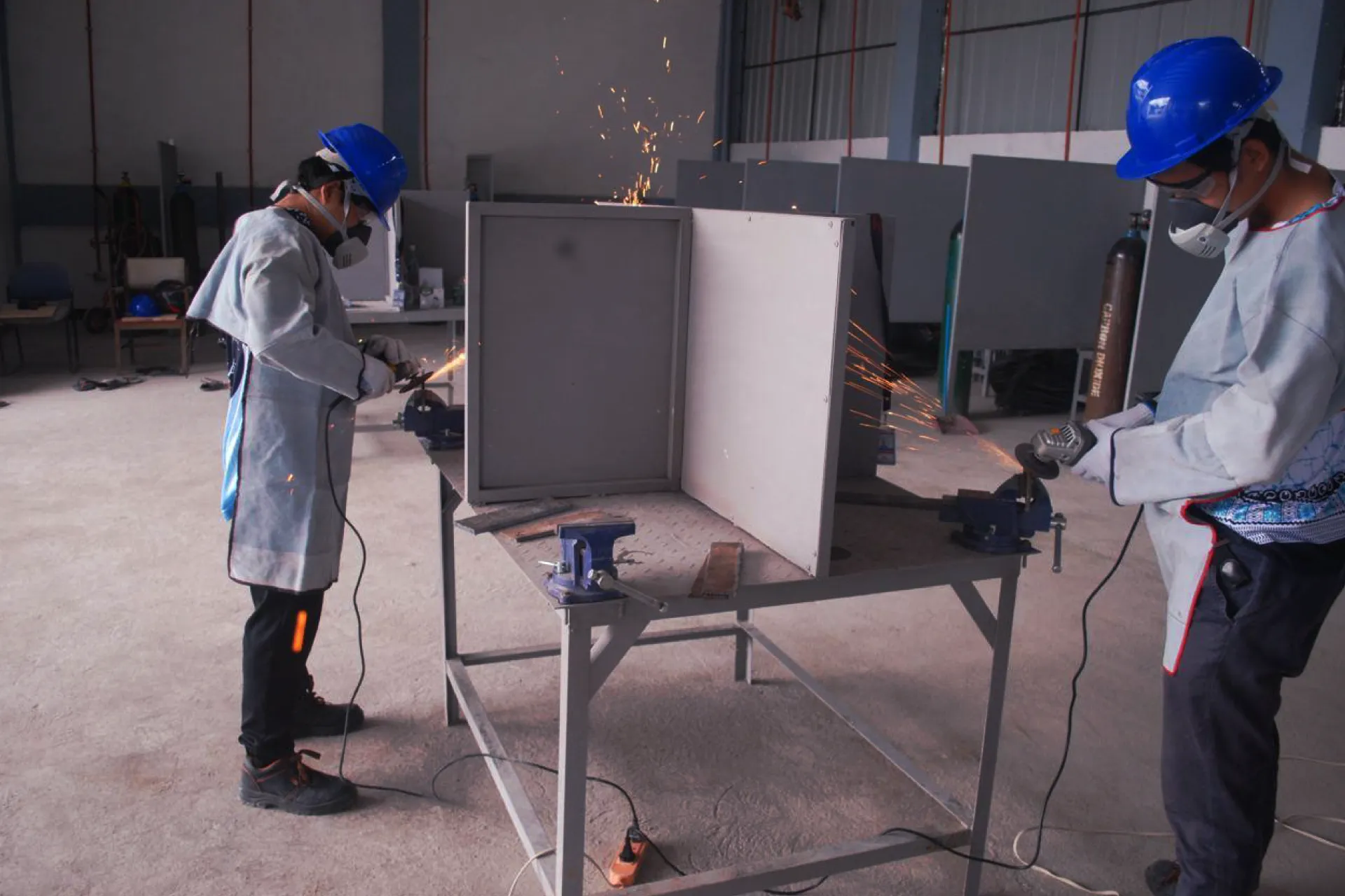 Two workers wearing safety glasses and respirators grinding metal with angle grinders