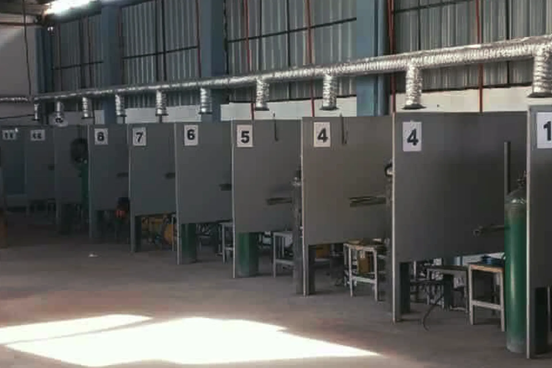 Row of equipped welding booths with individual exhaust ventilation in a training workshop.