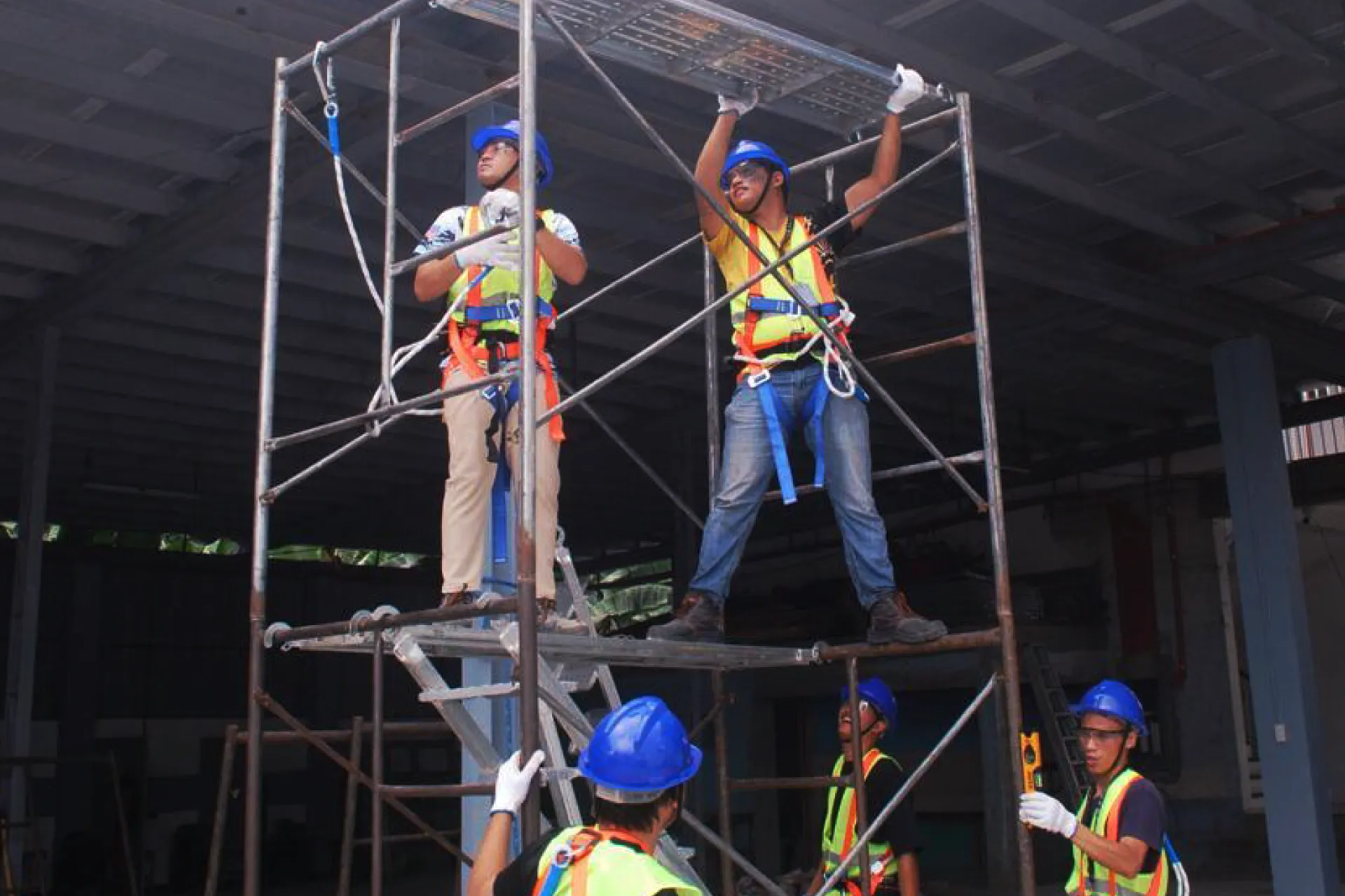 Workers wearing hard hats and safety harnesses assembling scaffolding at a height