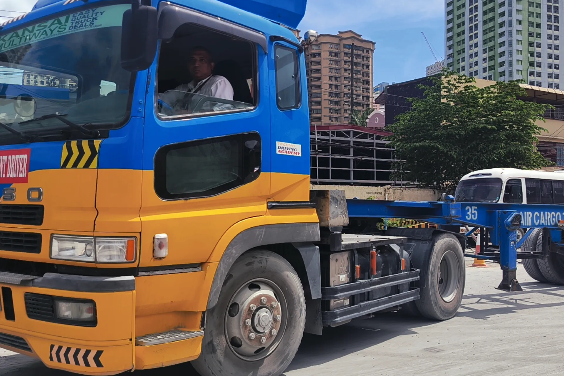 Close-up side view of a student driver sitting inside the cabin of a Techno Driving Academy truck