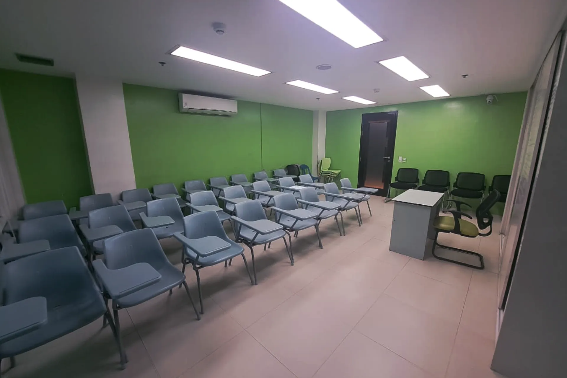 An empty classroom at a training center with green walls, rows of student chairs with desks, and an instructor's station.
