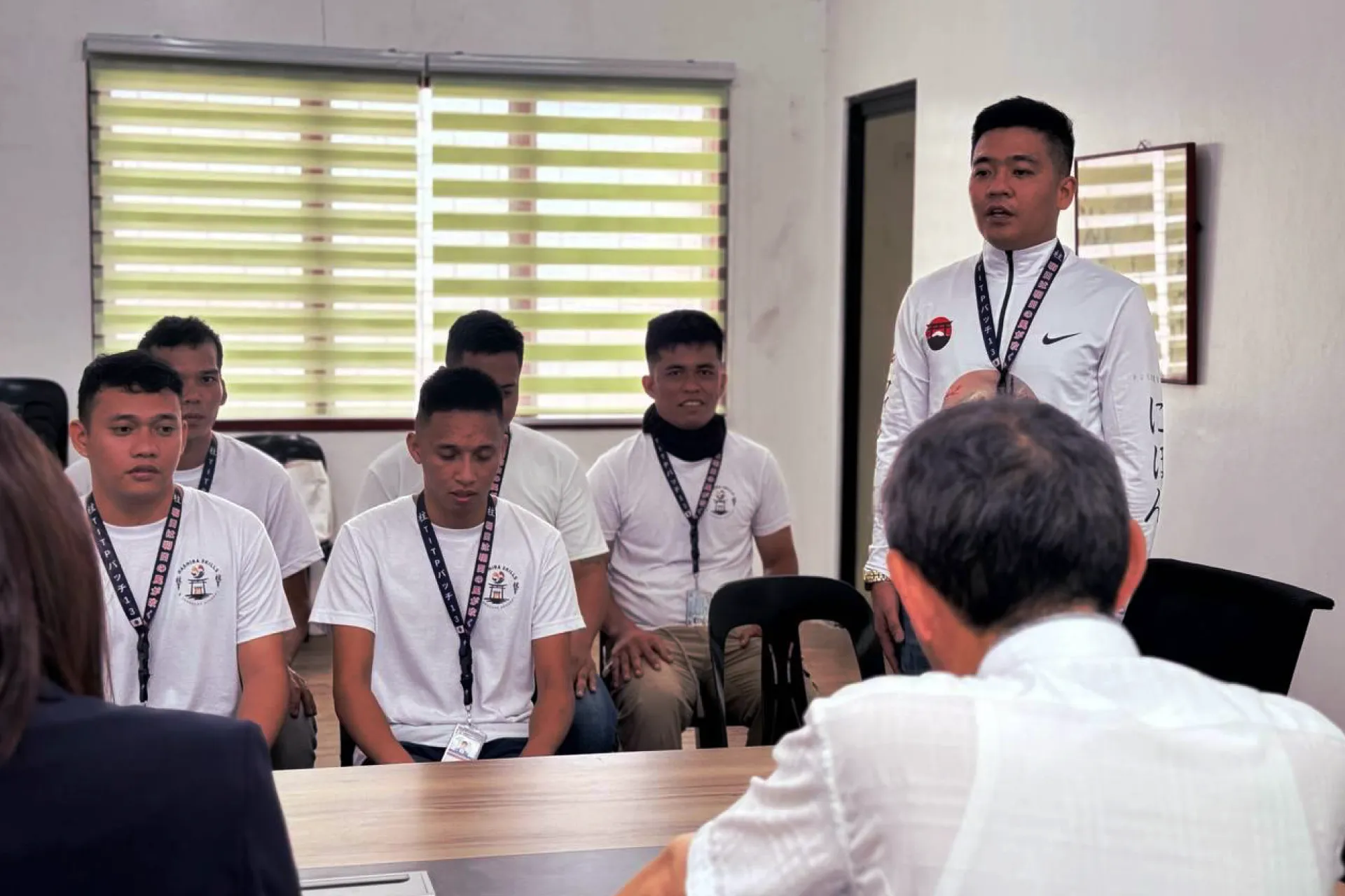A candidate facing an interview panel with interviewers at a desk featuring small Japanese and Philippine flags during a recruitment assessment.