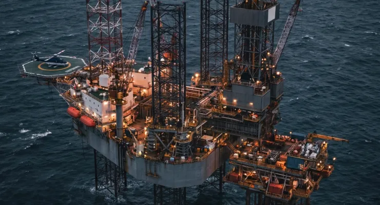 Offshore oil drilling rig platform with a helicopter pad in the middle of the ocean at twilight.