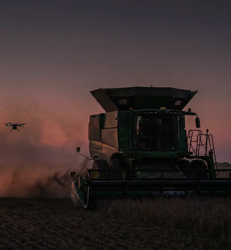 Smart farming concept showing a combine harvester working in a field at sunset accompanied by an agricultural drone.