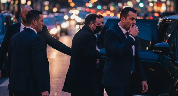Professional security guards in suits protecting a VIP entering a black car on a busy city street at night.