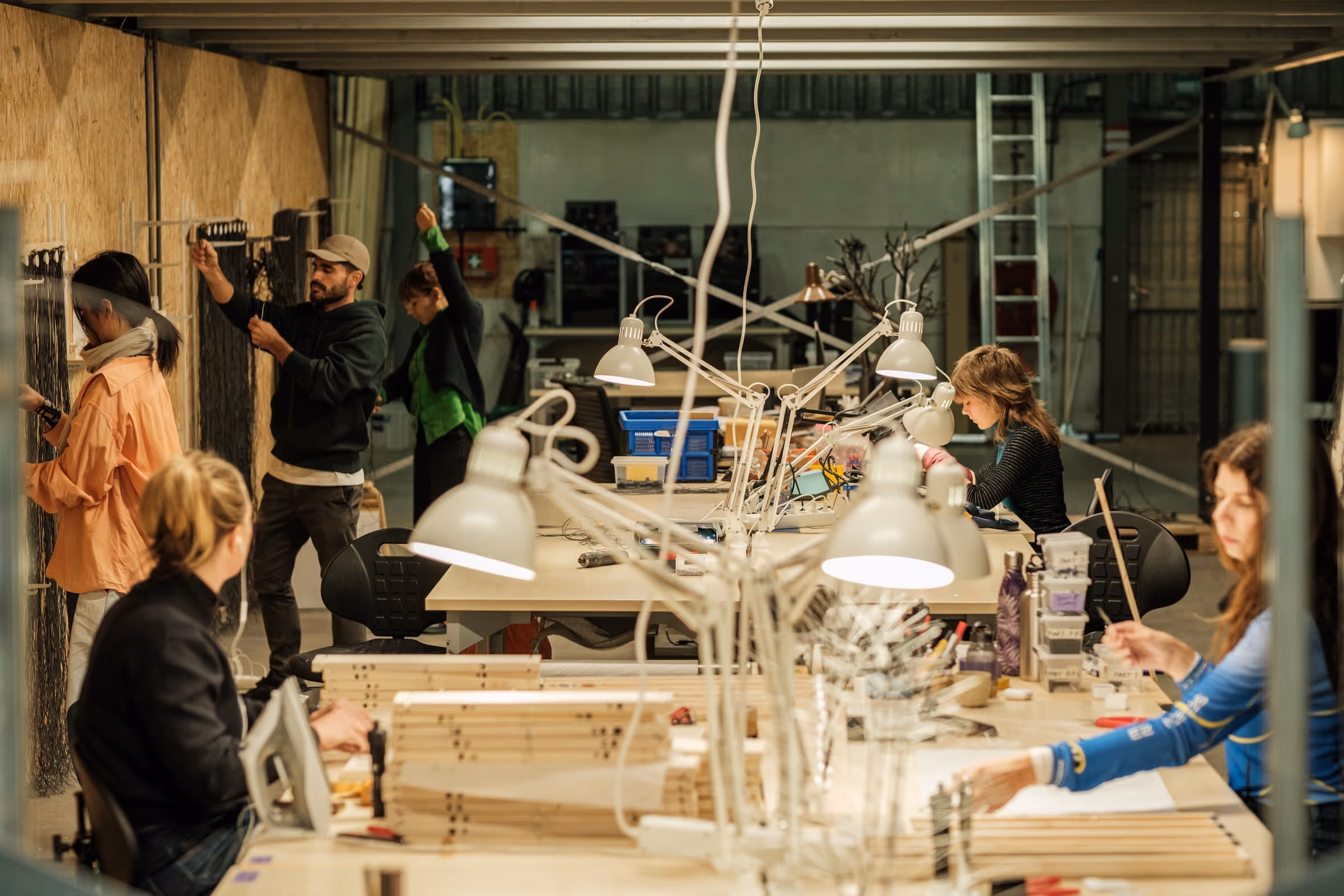 People working on Assembly projects in a well-lit workshop with tools and lamps on tables.