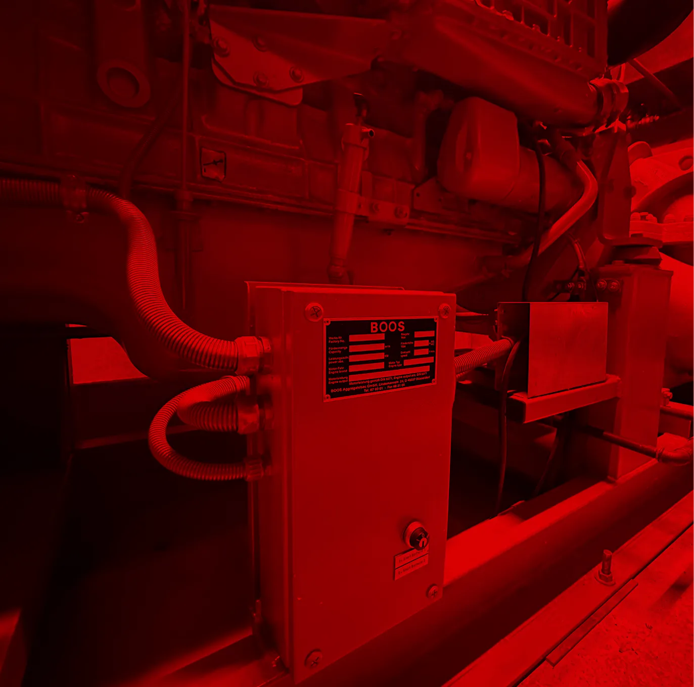Maschinenteil mit Steuerkasten und Kabeln in einer Industrieanlage, rot beleuchtet.