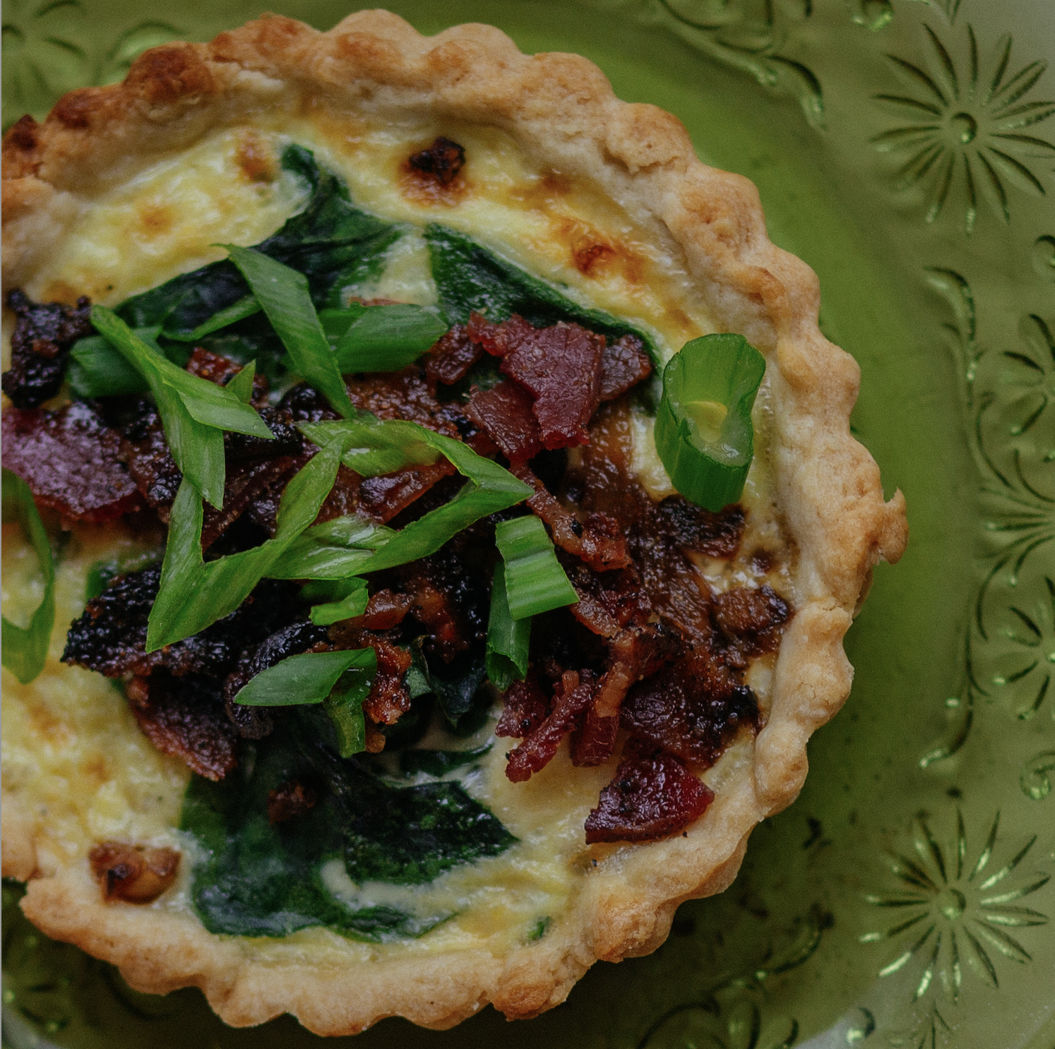 Spinach bacon quiche on a semi-opaque green plate