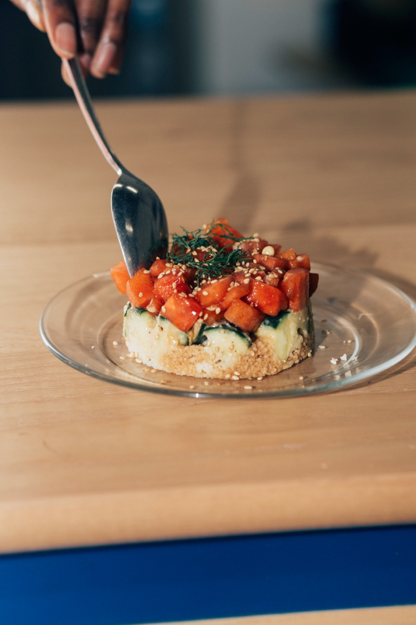 Glossy chopped watermelon tartare generously piled atop a bed of layered cucumber and rice, sprinkled with chopped dill and sesame seeds.