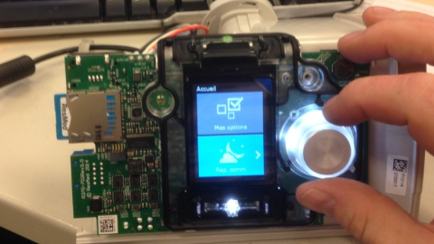 Close-up of a hand adjusting a control knob on an open electronic device with a small screen displaying a menu in French.