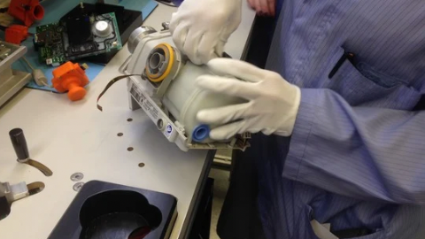 Person wearing gloves assembling or inspecting a ResMed AirSense 10 CPAP device on a workbench.