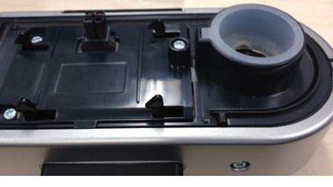 Close-up of a ResMed alarm module showing black plastic casing, metal screws, and a gray circular component.