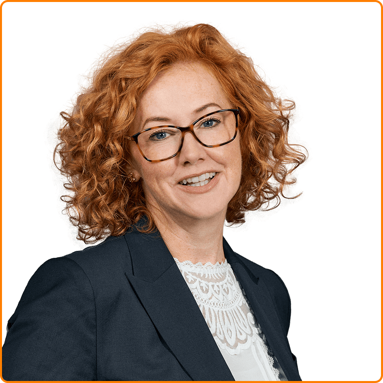Smiling woman with curly red hair wearing glasses, a white lace top, and a dark blazer.