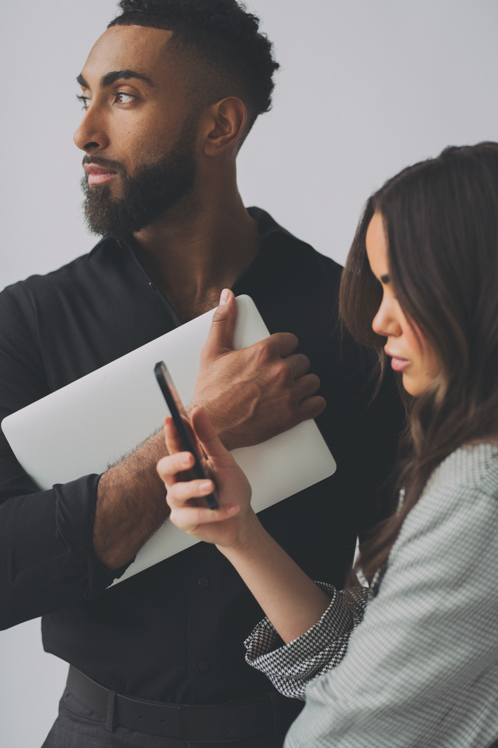  A man holding a laptop while a woman beside him looks at her smartphone 