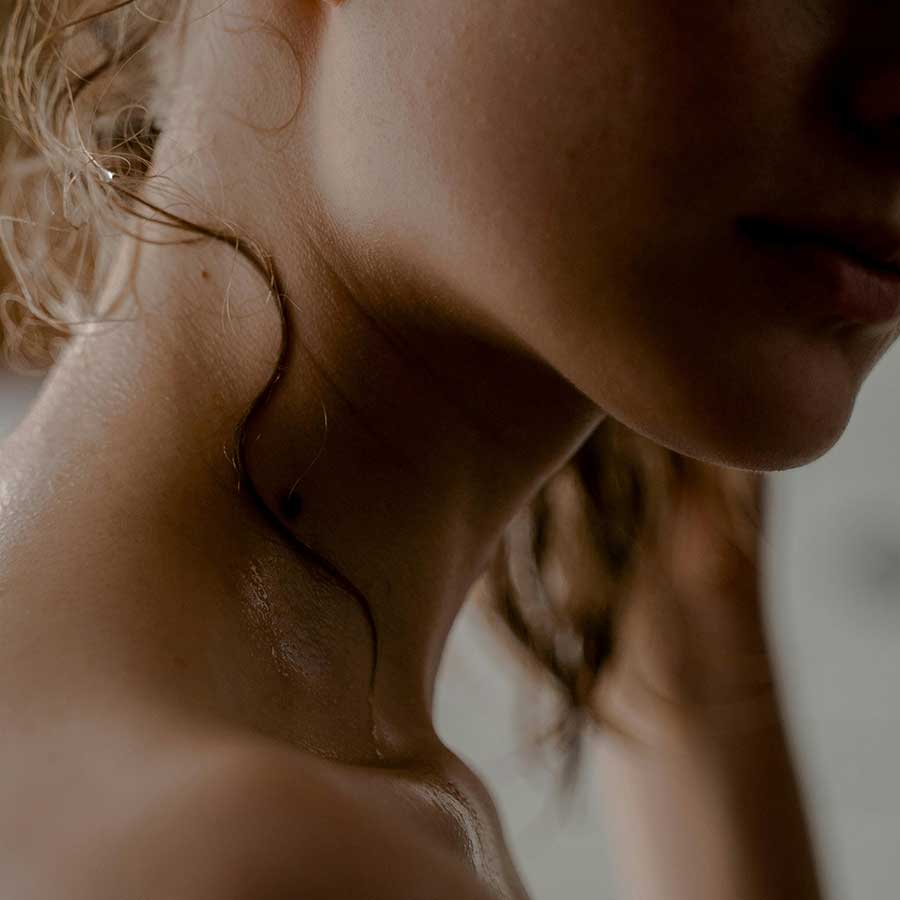 Close-up of a woman's neck and jawline with a strand of curly hair resting on her neck.