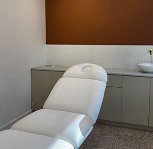 White treatment chair in a minimalist spa room with beige cabinets and a brown accent wall.