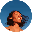 Smiling person with long hair blowing in the wind against a clear blue sky.