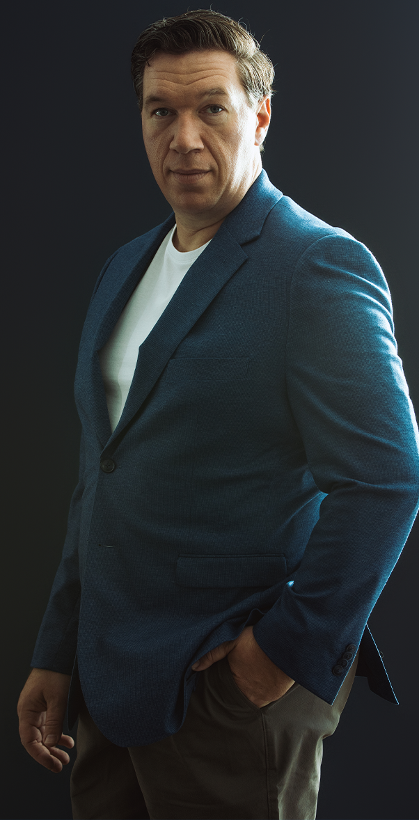 Portrait of Topher Field wearing a blue blazer, standing against a dark background.