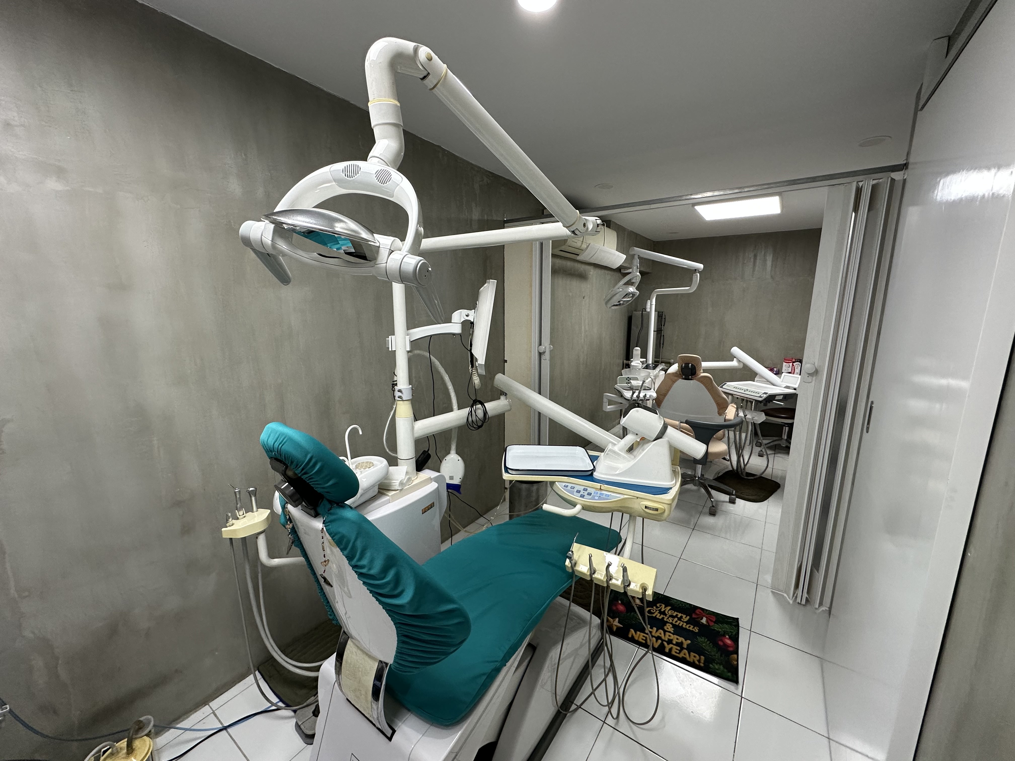 Modern dental clinic with two dental chairs and overhead dental lights in rooms with gray walls and white tiled floors inside Umbrella Dental Clinic.