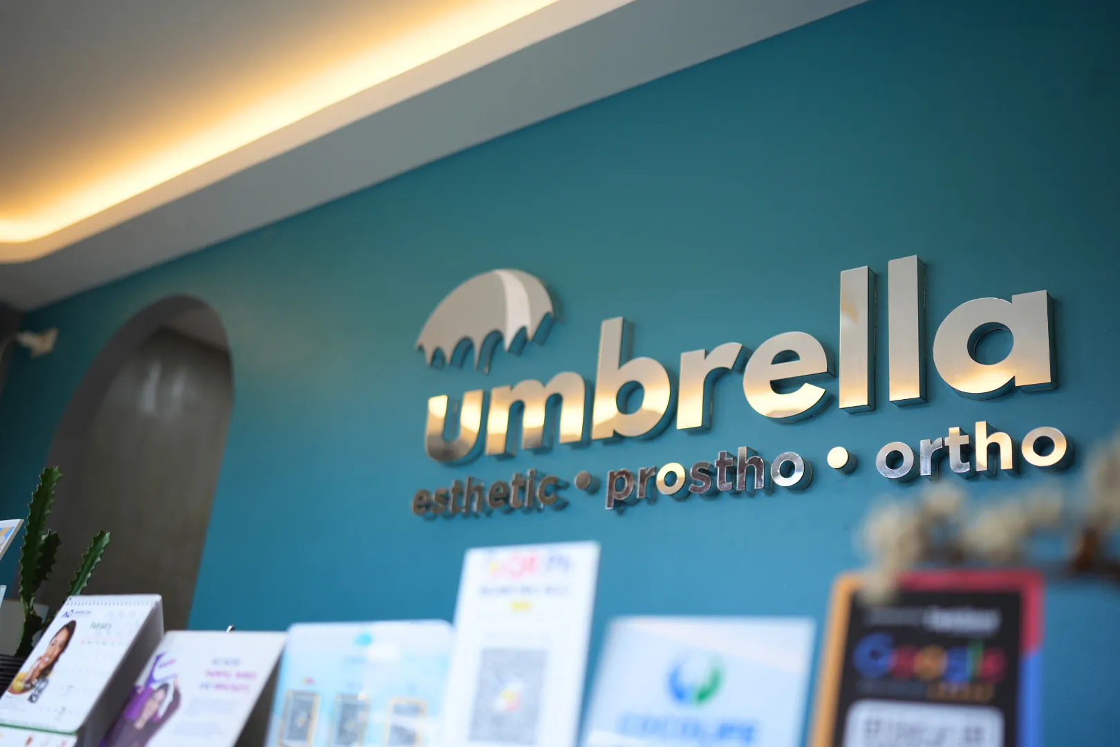 Reception of Umbrella Dental Clinic area with a decorated Christmas tree, green sofa, wooden coffee table with plants, and a counter adorned with Christmas decorations under an Umbrella dental clinic sign.