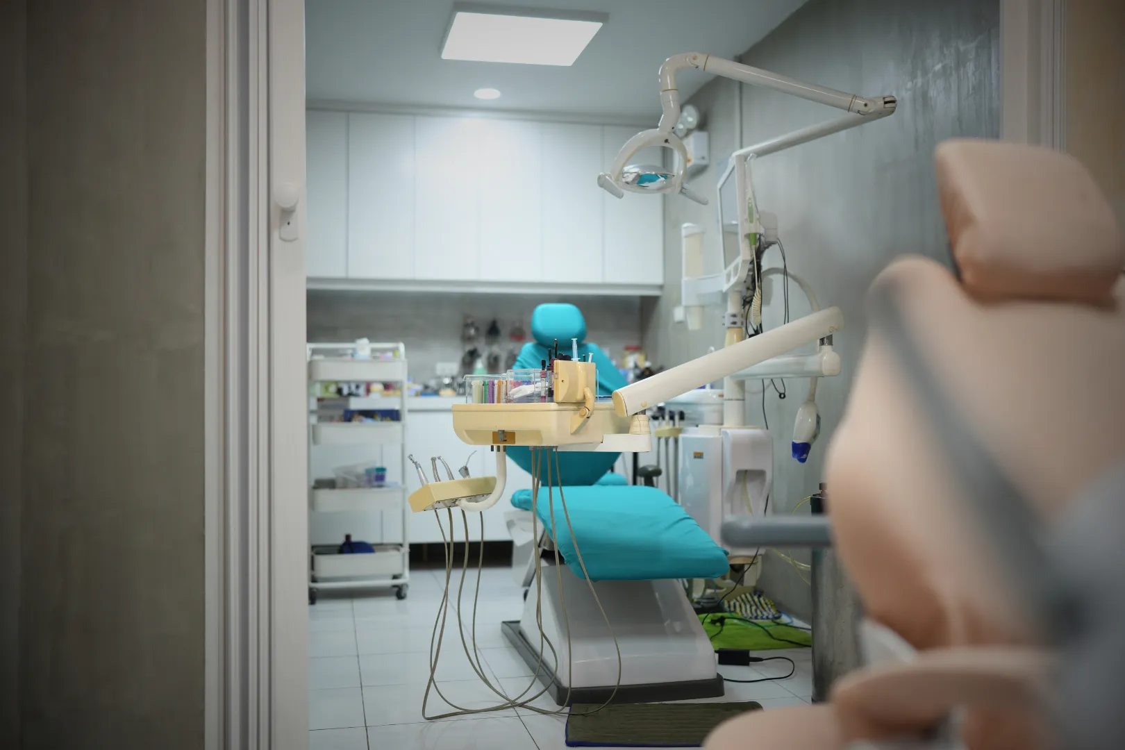 Waiting area of Umbrella Dental Clinic with black metal chairs, wooden side table with documents, a Christmas wreath on a gray wall, and a decorated Christmas tree visible through an archway.