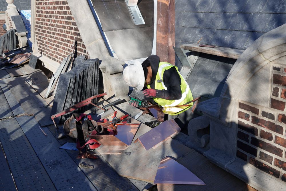 A man is installing a slate roof with copper step flashing.