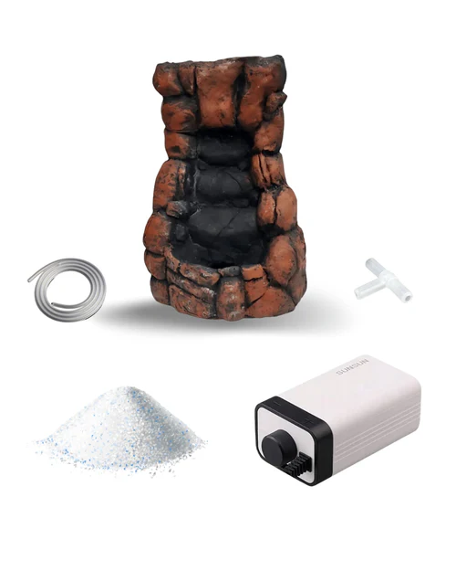 Rock-style tabletop water fountain with a coil tube, T-shaped connector, white granular material, and a small white pump with a black dial.