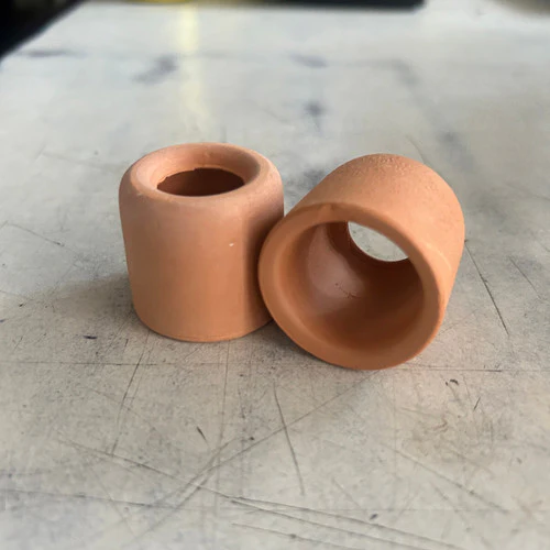 Two small cylindrical terracotta-colored clay pieces with hollow centers on a scratched surface.