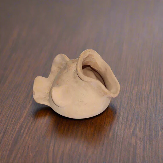 Small, abstract beige clay sculpture with curved forms on a wooden surface.
