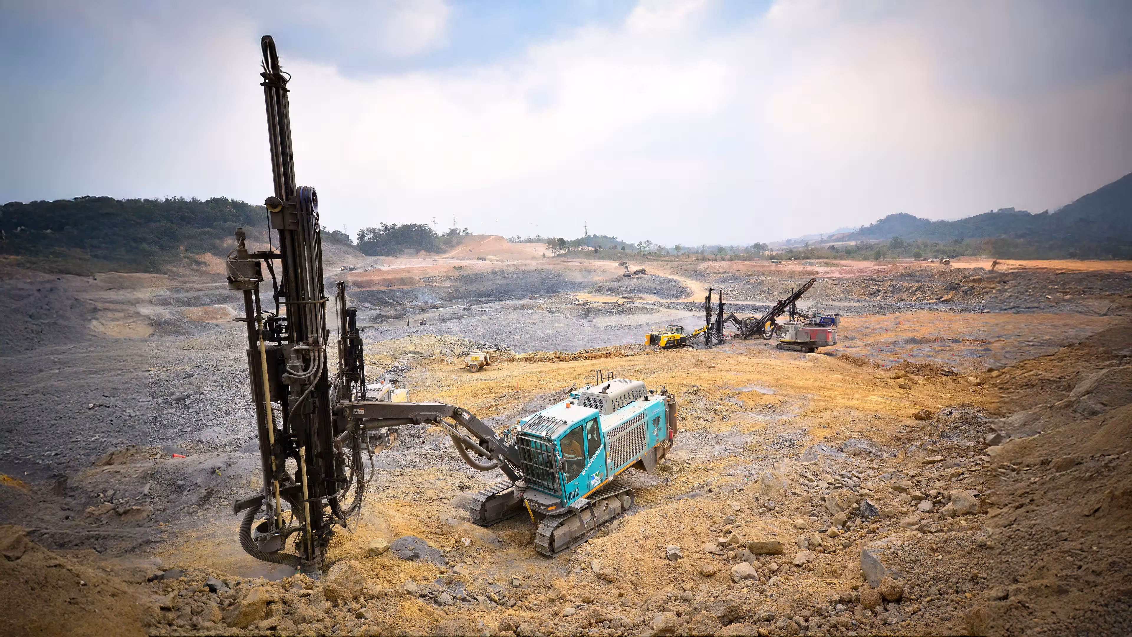 Construction machinery working on a dirt road in a mountainous area under a clear blue sky.