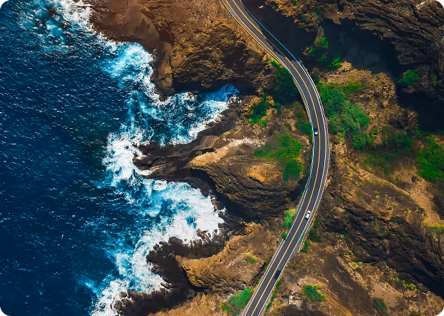 Aerial view of a coastal road winding along rocky cliffs with waves crashing against the shore.