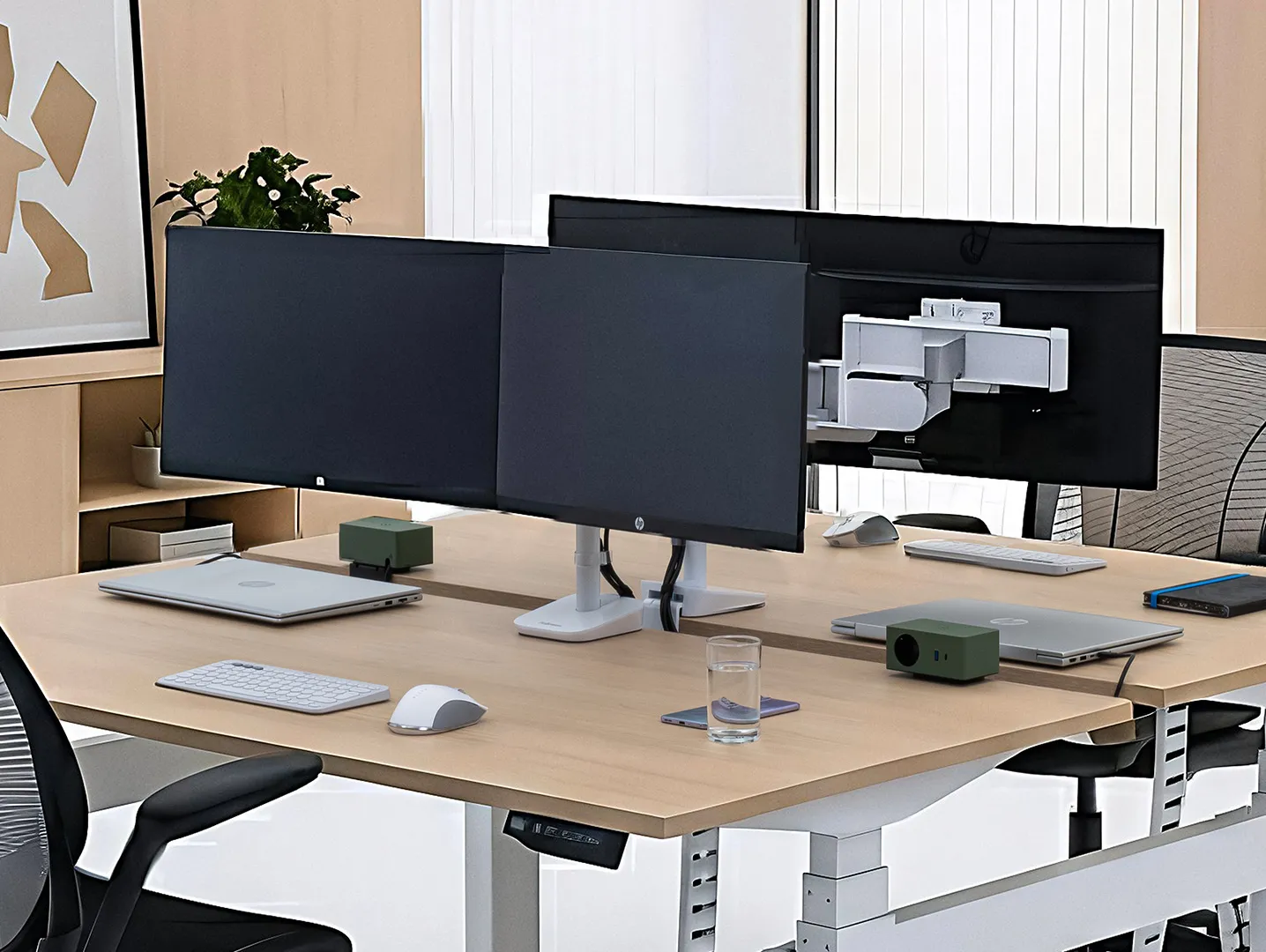 Twee bureaus met dubbele monitorarmen, laptops, en kantoormateriaal in een lichte kantoorruimte.