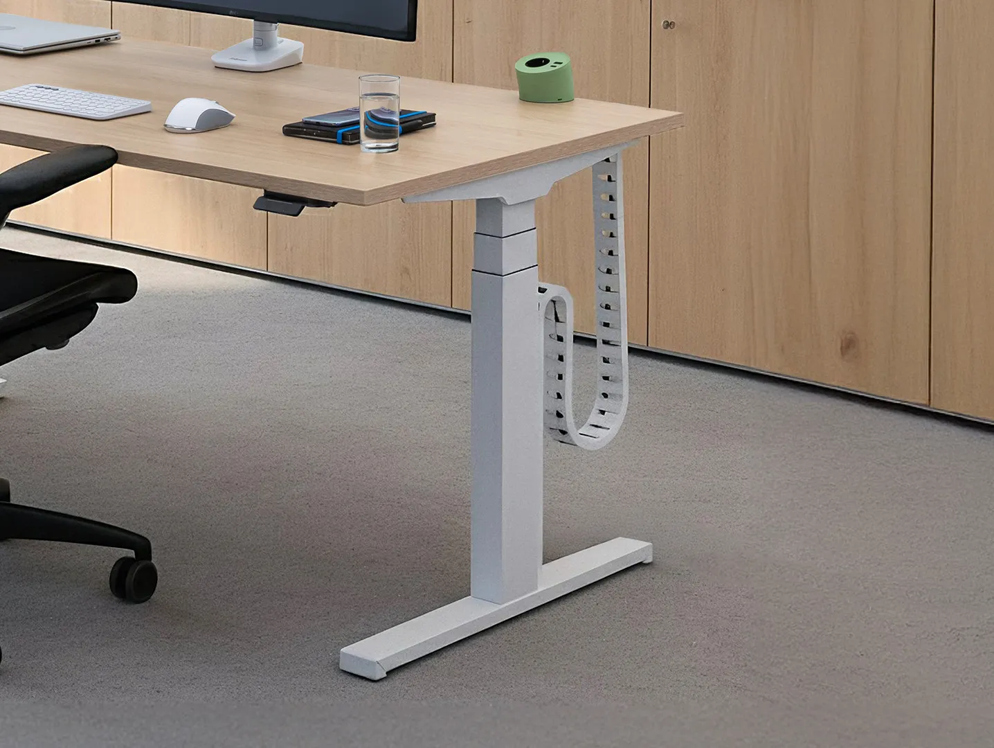 Bureau met licht houten blad en wit verstelbaar onderstel, kabelmanagementlus eraan bevestigd, met bureaustoel, muis, toetsenbord, glazen water en elektronische apparaten erop.