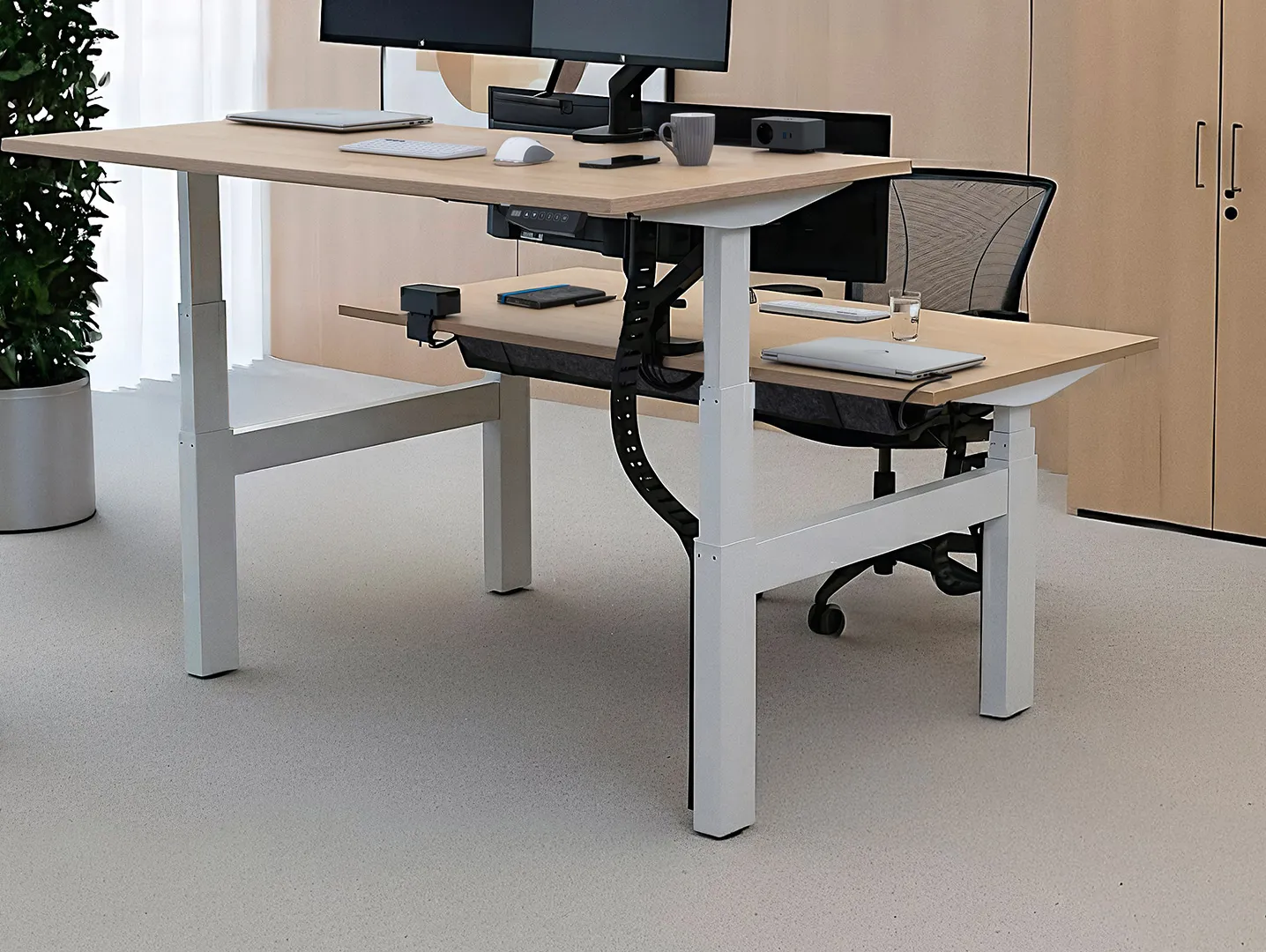 Werkplek met bureau met twee verstelbare monitoren, laptop, muis, toetsenbord, koffiekopje, en bureaustoel in een lichte kantoorruimte.